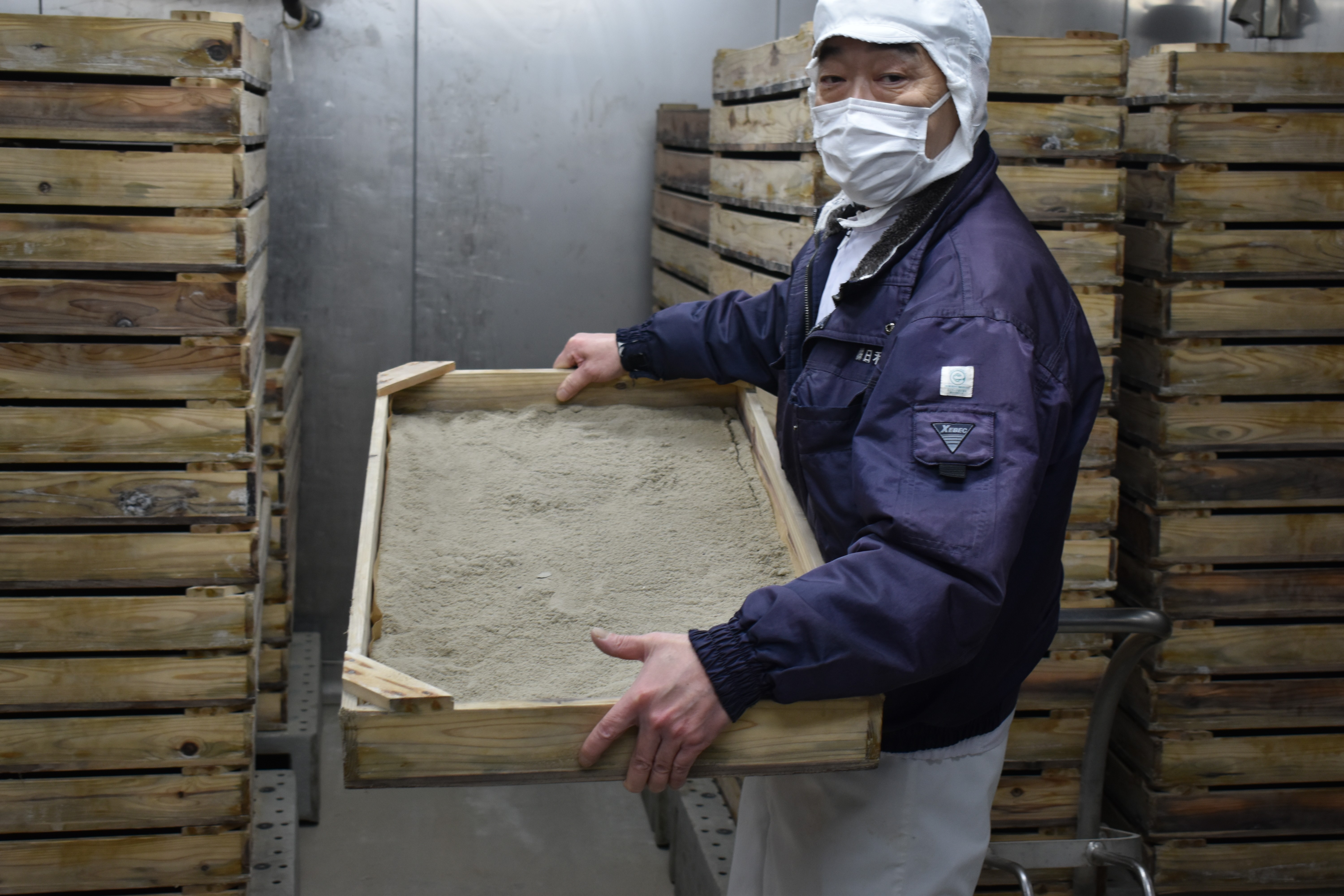 火山灰が入った木枠を持つ橋元さん